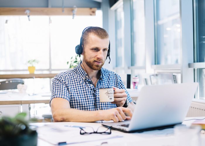man-with-cup-headsetworking-laptop